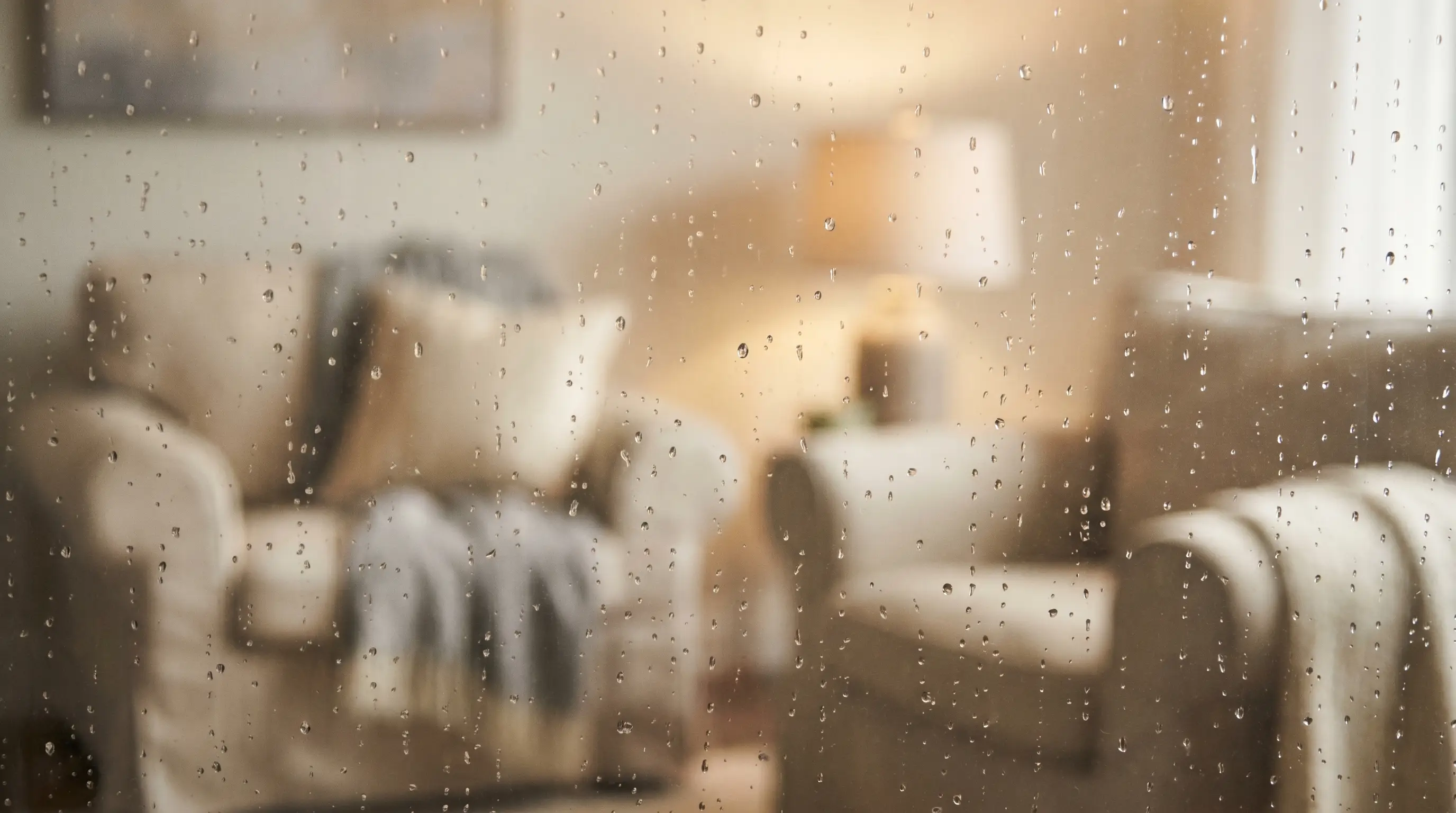 Rain droplets on a window pane with a blurred warm interior behind it